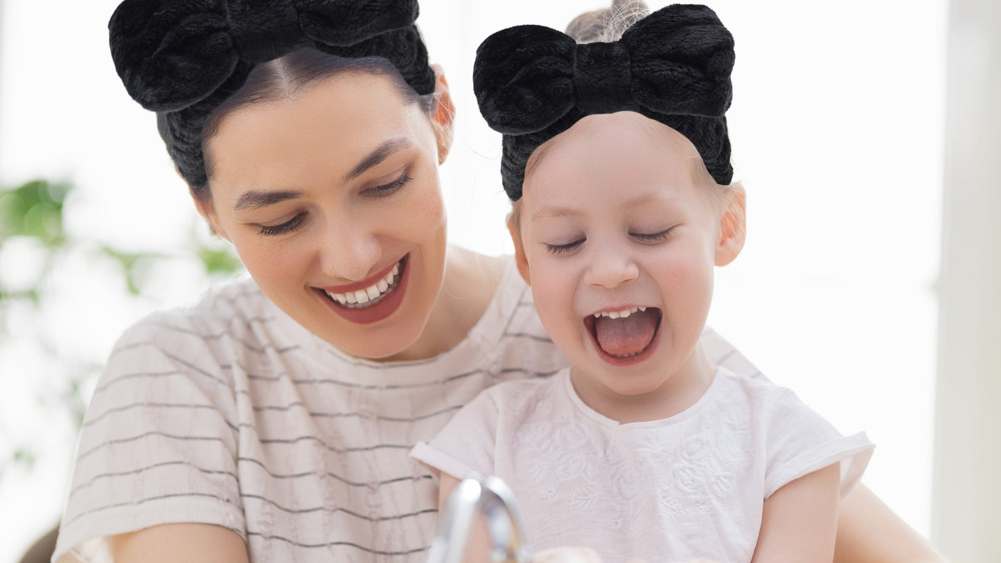 Woman and child with black bows on head washing faces indoors.
